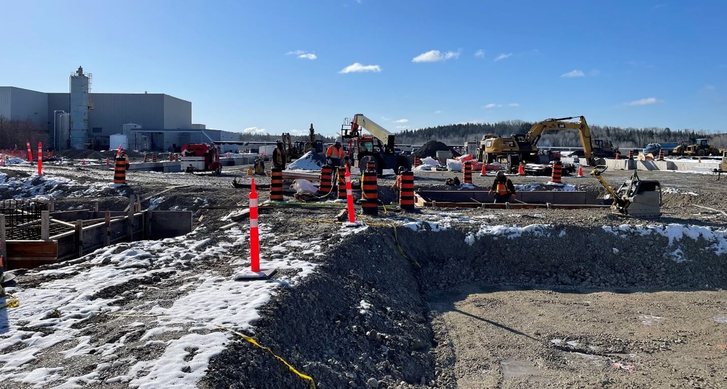 Crews working within the foundation walls of the new solvent extraction building, installing support for SX tanks and steel structures. Existing refinery building can be seen in the background. 